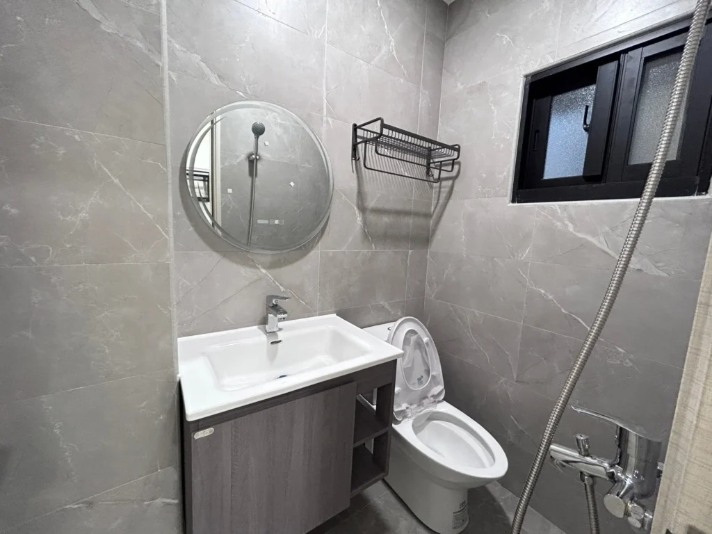 建工路老屋翻新衛浴，灰色石紋磁磚搭配圓形鏡面與木紋懸掛浴櫃